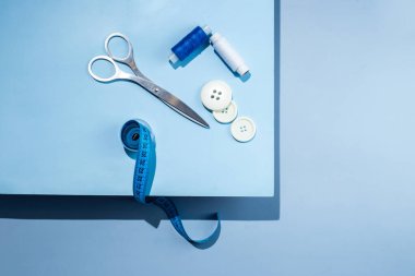 Aksesuar dikiyorum. İplikler, makas, mezura, mavi arkaplandaki düğmeler