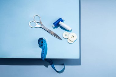 Aksesuar dikiyorum. İplikler, makas, mezura, mavi arkaplandaki düğmeler