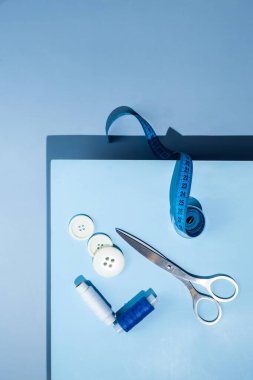 Aksesuar dikiyorum. İplikler, makas, mezura, mavi arkaplandaki düğmeler