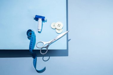 Aksesuar dikiyorum. İplikler, makas, mezura, mavi arkaplandaki düğmeler