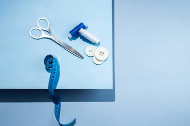 Aksesuar dikiyorum. İplikler, makas, mezura, mavi arkaplandaki düğmeler