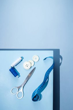 Aksesuar dikiyorum. İplikler, makas, mezura, mavi arkaplandaki düğmeler