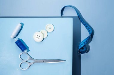 Aksesuar dikiyorum. İplikler, makas, mezura, mavi arkaplandaki düğmeler