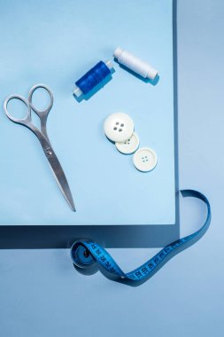 Aksesuar dikiyorum. İplikler, makas, mezura, mavi arkaplandaki düğmeler