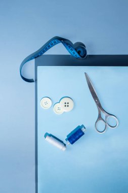 Aksesuar dikiyorum. İplikler, makas, mezura, mavi arkaplandaki düğmeler