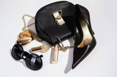 Beyaz yüzeyde zarif siyah çanta, yüksek topuklu ayakkabı ve kozmetik ürünler..