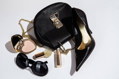 Beyaz yüzeyde zarif siyah çanta, yüksek topuklu ayakkabı ve kozmetik ürünler..