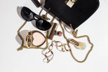 Beyaz yüzeyde zarif siyah çanta, yüksek topuklu ayakkabı ve kozmetik ürünler..
