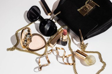 Beyaz yüzeyde zarif siyah çanta, yüksek topuklu ayakkabı ve kozmetik ürünler..