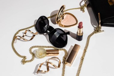 Beyaz yüzeyde zarif siyah çanta, yüksek topuklu ayakkabı ve kozmetik ürünler..