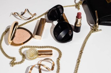 Beyaz yüzeyde zarif siyah çanta, yüksek topuklu ayakkabı ve kozmetik ürünler..