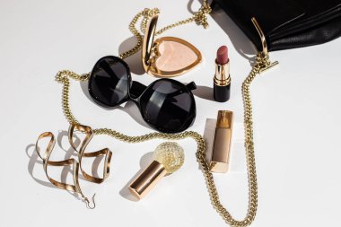 Beyaz yüzeyde zarif siyah çanta, yüksek topuklu ayakkabı ve kozmetik ürünler..