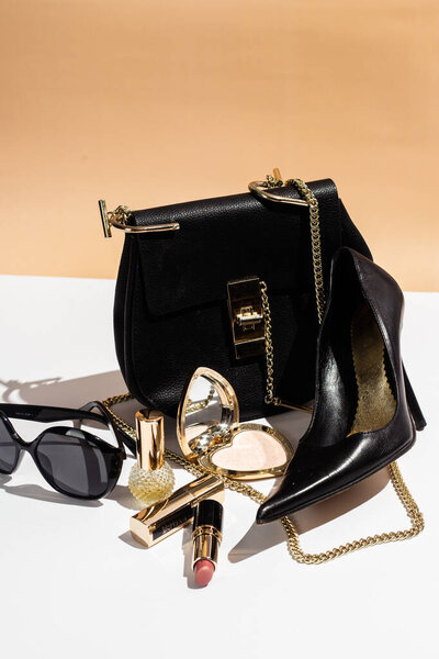 Элегантная черная сумка, высокие каблуки и косметика на белой поверхности.