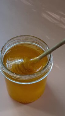 Bal yavaşça sarı arka planda bal kaşığından damlıyor.