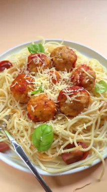 Köfteli spagetti, domates soslu, beyaz tabakta peynirli, bej arka planda.
