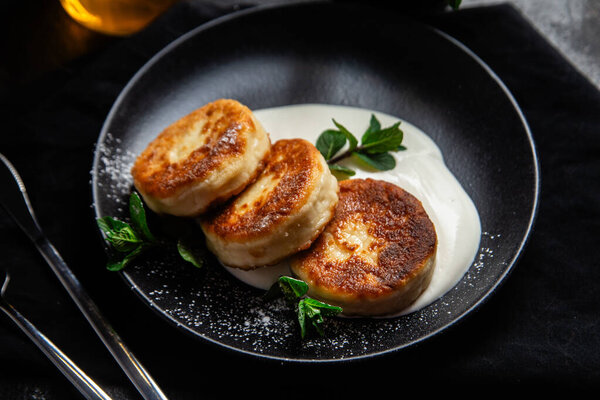 Чизкейки со сливочным соусом и мятой в черной тарелке на столе. Завтрак