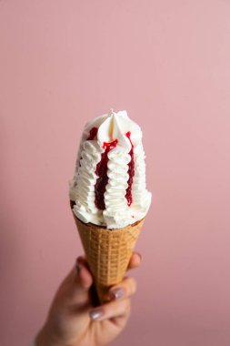 Bir kadının eli lezzetli bir dondurma külahını tutuyor. Krem şantili ve çilek soslu.