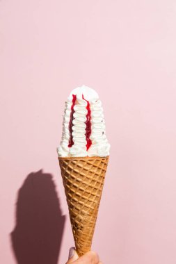 Bir kadının eli lezzetli bir dondurma külahını tutuyor. Krem şantili ve çilek soslu.