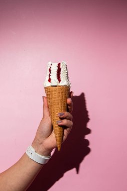 Bir kadının eli lezzetli bir dondurma külahını tutuyor. Krem şantili ve çilek soslu.