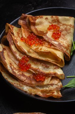 Masanın üzerinde siyah bir tabakta kırmızı havyarlı gözleme. Kahvaltı Maslenitsa