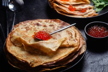 Masanın üzerinde siyah bir tabakta kırmızı havyarlı gözleme. Kahvaltı Maslenitsa