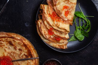 Masanın üzerinde siyah bir tabakta kırmızı havyarlı gözleme. Kahvaltı Maslenitsa