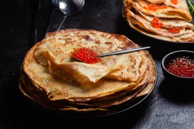 Masanın üzerinde siyah bir tabakta kırmızı havyarlı gözleme. Kahvaltı Maslenitsa