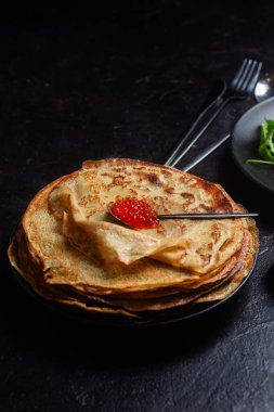 Masanın üzerinde siyah bir tabakta kırmızı havyarlı gözleme. Kahvaltı Maslenitsa