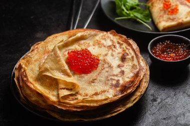 Masanın üzerinde siyah bir tabakta kırmızı havyarlı gözleme. Kahvaltı Maslenitsa