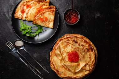 Masanın üzerinde siyah bir tabakta kırmızı havyarlı gözleme. Kahvaltı Maslenitsa