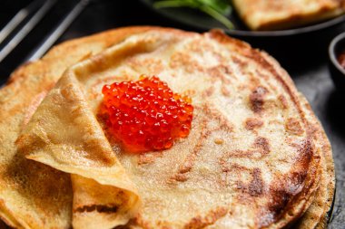 Masanın üzerinde siyah bir tabakta kırmızı havyarlı gözleme. Kahvaltı Maslenitsa