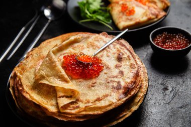 Masanın üzerinde siyah bir tabakta kırmızı havyarlı gözleme. Kahvaltı Maslenitsa