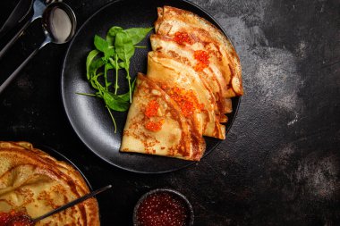 Masanın üzerinde siyah bir tabakta kırmızı havyarlı gözleme. Kahvaltı Maslenitsa