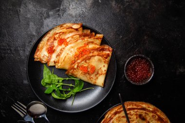 Masanın üzerinde siyah bir tabakta kırmızı havyarlı gözleme. Kahvaltı Maslenitsa