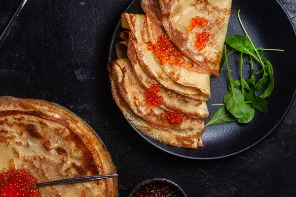 Masanın üzerinde siyah bir tabakta kırmızı havyarlı gözleme. Kahvaltı Maslenitsa