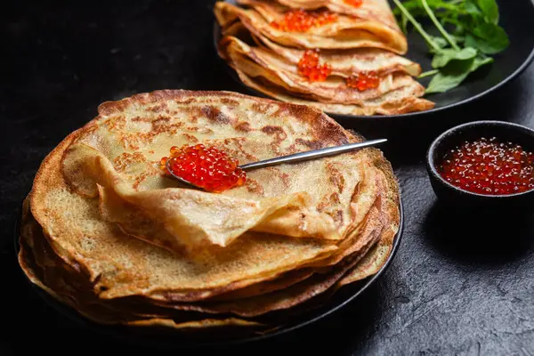 Masanın üzerinde siyah bir tabakta kırmızı havyarlı gözleme. Kahvaltı Maslenitsa