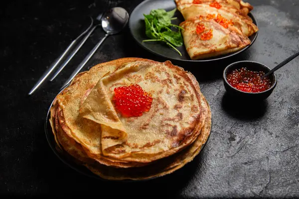 Masanın üzerinde siyah bir tabakta kırmızı havyarlı gözleme. Kahvaltı Maslenitsa