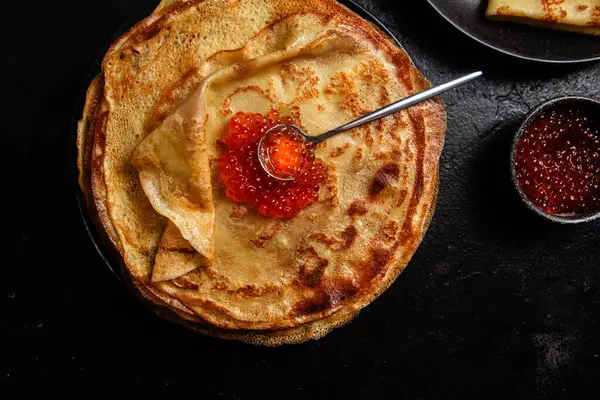 Masanın üzerinde siyah bir tabakta kırmızı havyarlı gözleme. Kahvaltı Maslenitsa
