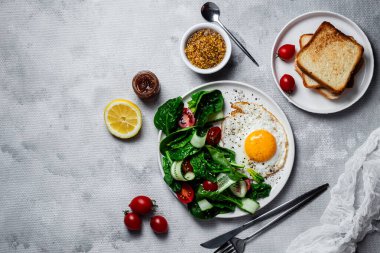 Beyaz tabakta ıspanaklı yumurta, domates ve salatalık salatası. Sağlıklı kahvaltı.