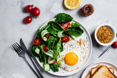 Beyaz tabakta ıspanaklı yumurta, domates ve salatalık salatası. Sağlıklı kahvaltı.