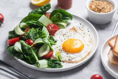 Beyaz tabakta ıspanaklı yumurta, domates ve salatalık salatası. Sağlıklı kahvaltı.