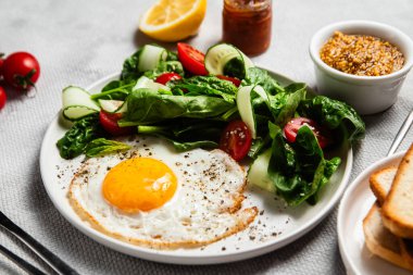 Beyaz tabakta ıspanaklı yumurta, domates ve salatalık salatası. Sağlıklı kahvaltı.