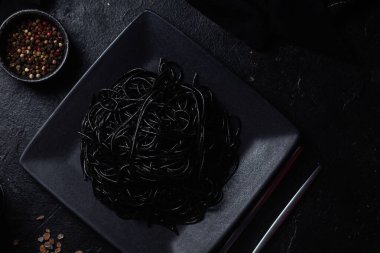 Siyah bir tabakta siyah bir arka planda siyah spagetti. Mürekkep balıklı siyah macun.