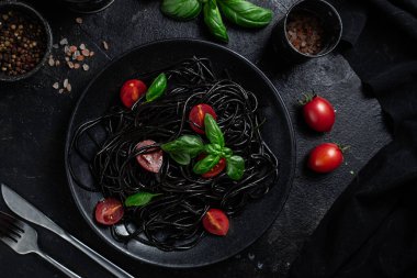 Vişneli siyah spagetti ve siyah arka planda siyah bir tabakta fesleğen..