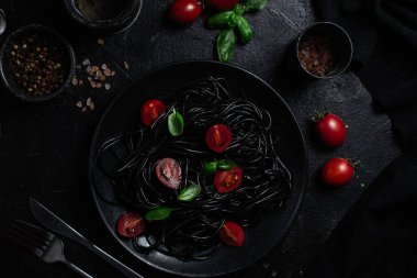 Vişneli siyah spagetti ve siyah arka planda siyah bir tabakta fesleğen..