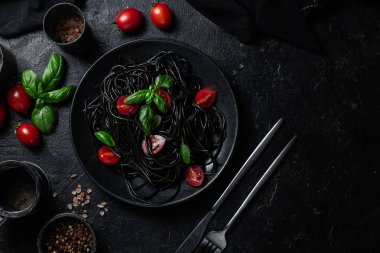 Vişneli siyah spagetti ve siyah arka planda siyah bir tabakta fesleğen..