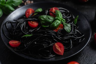 Vişneli siyah spagetti ve siyah arka planda siyah bir tabakta fesleğen..