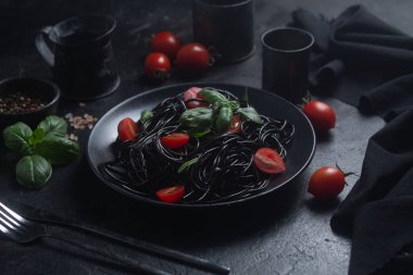 Vişneli siyah spagetti ve siyah arka planda siyah bir tabakta fesleğen..