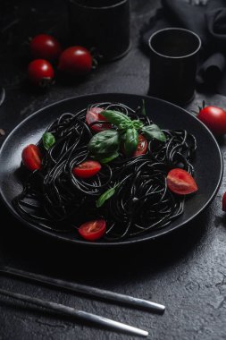 Vişneli siyah spagetti ve siyah arka planda siyah bir tabakta fesleğen..