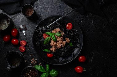 Ton balıklı siyah spagetti, vişneli domates ve siyah bir tabakta fesleğen..